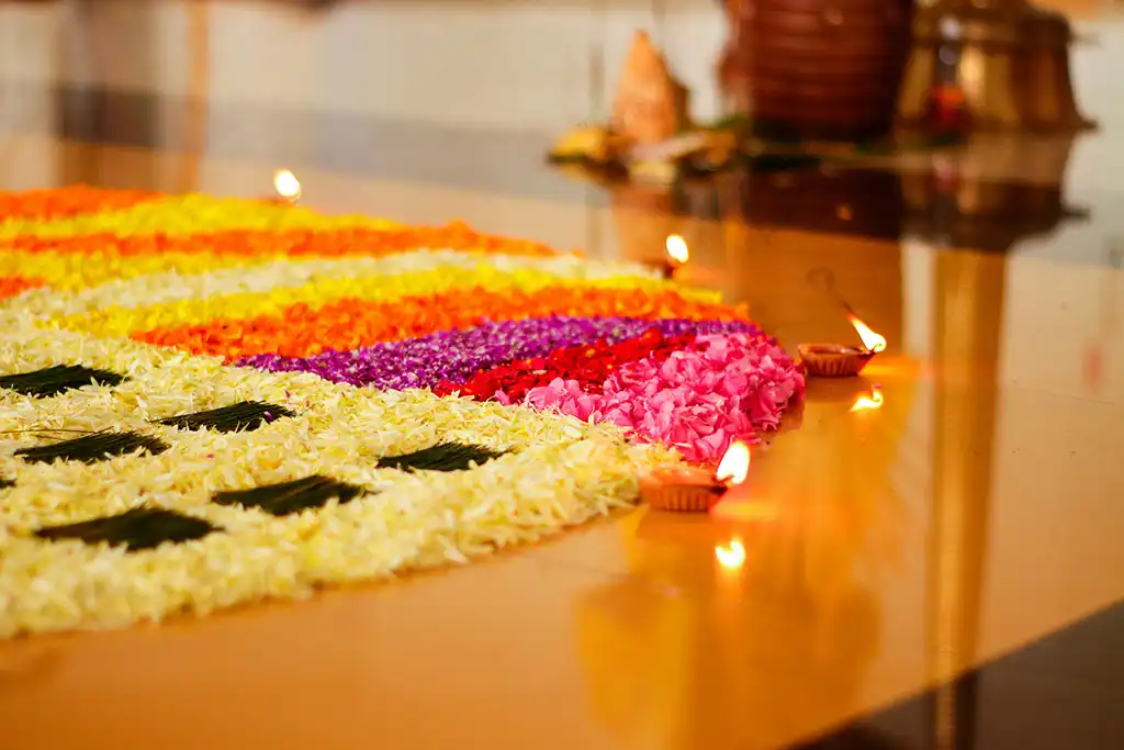 A large pookalam of coloured flower petals surrounded by lit oil lamps